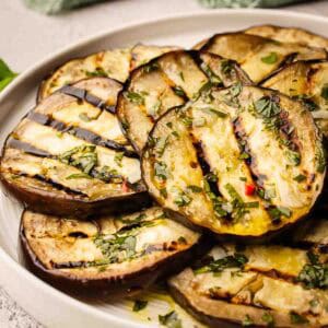 Grilled eggplant slices piled onto a round plate.