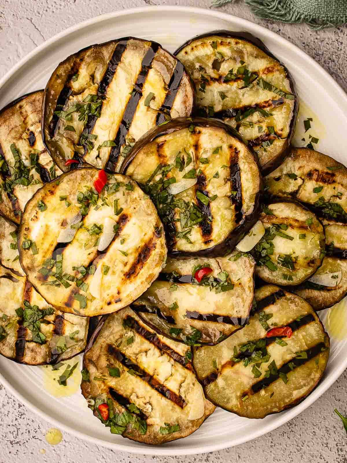 Grilled eggplant slices piled onto a round plate viewed from above.