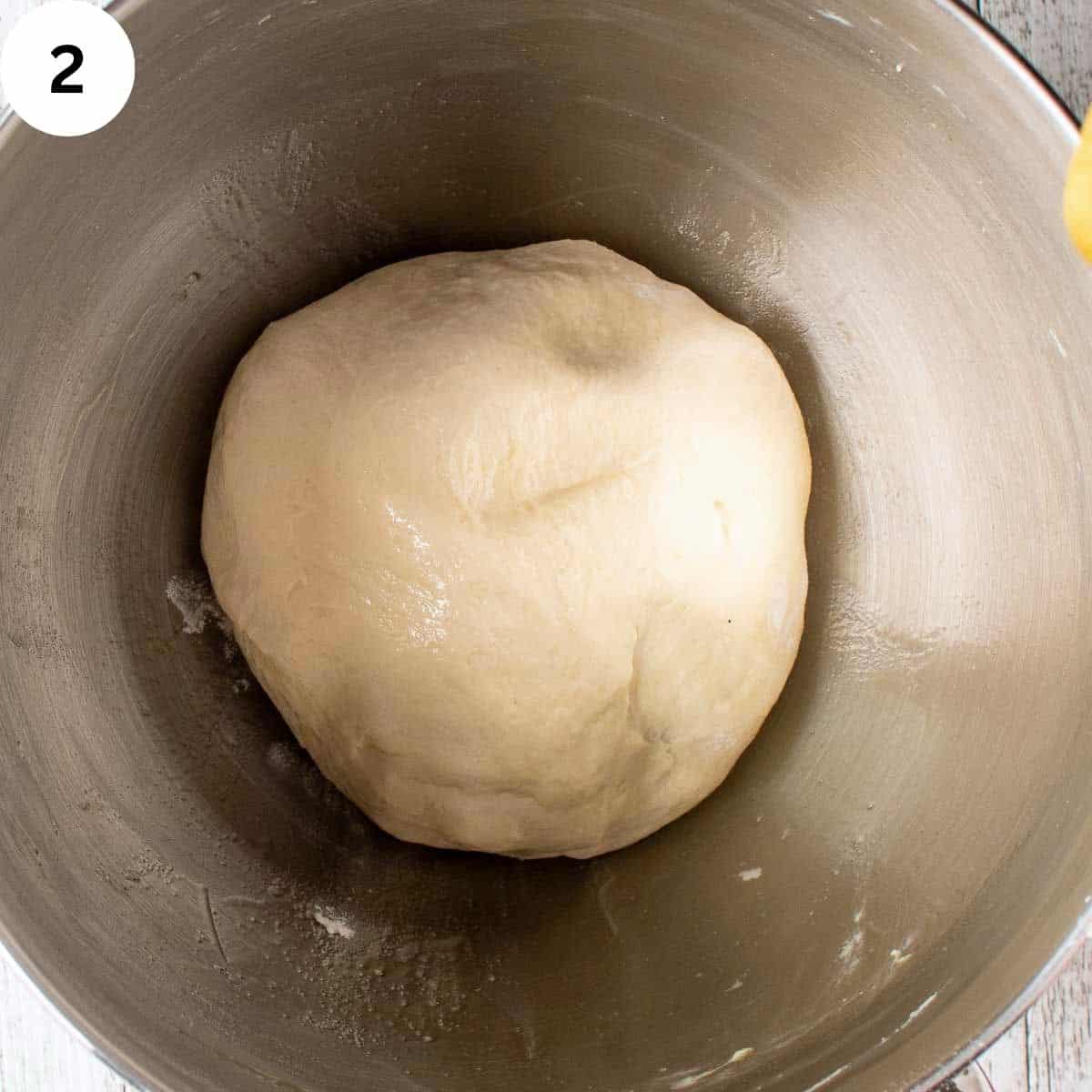 Pizza dough kneaded and ready to rise in a stainless steel bowl.