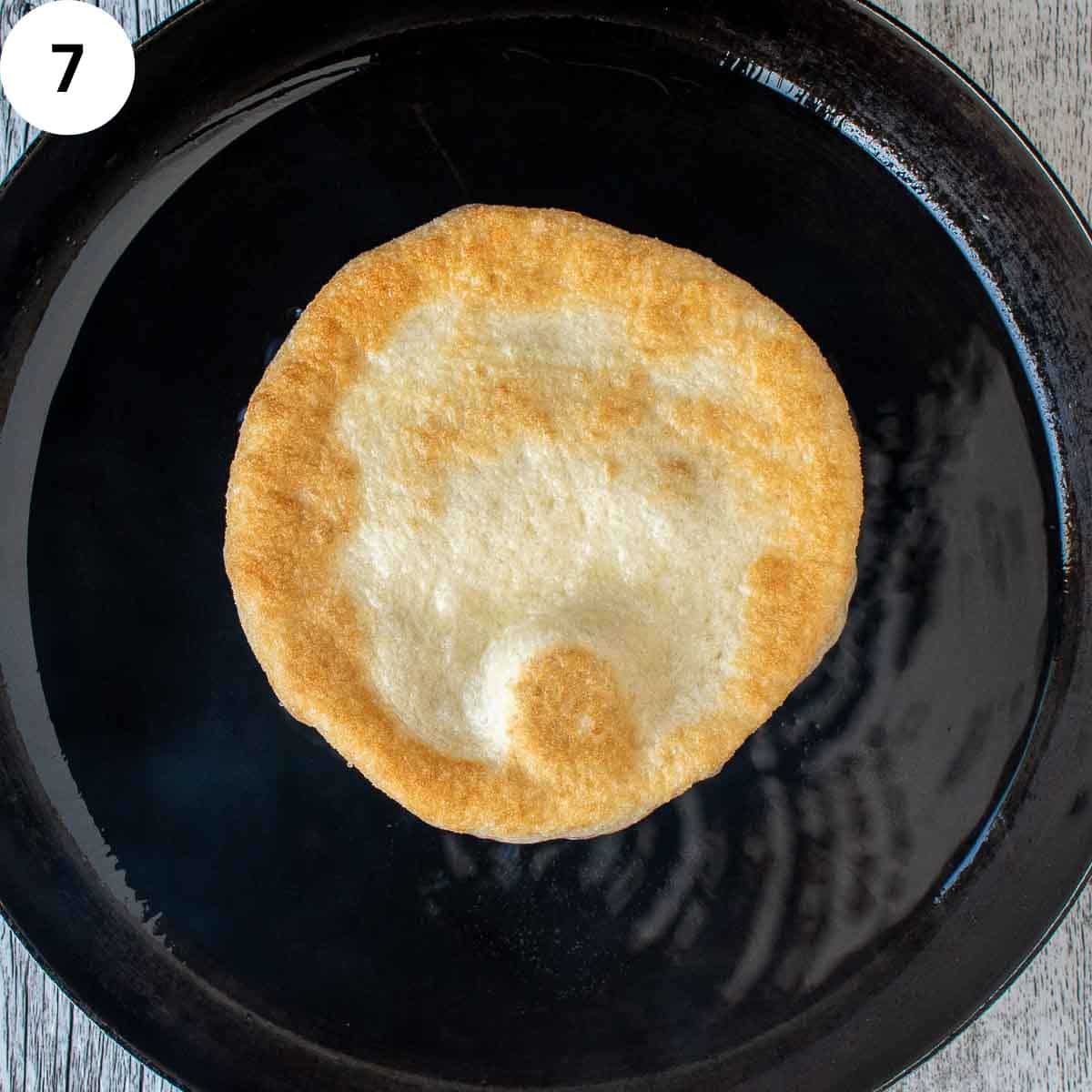 Disk of pizza dough fried in a skillet.