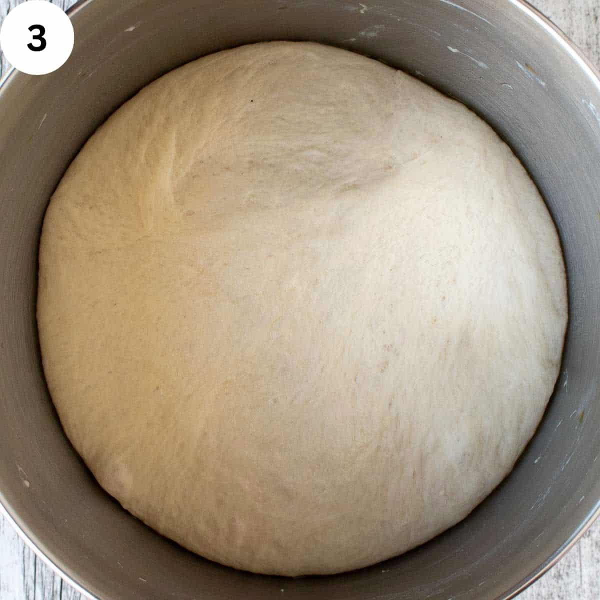 Risen yeasted dough in a stainless steel bowl.