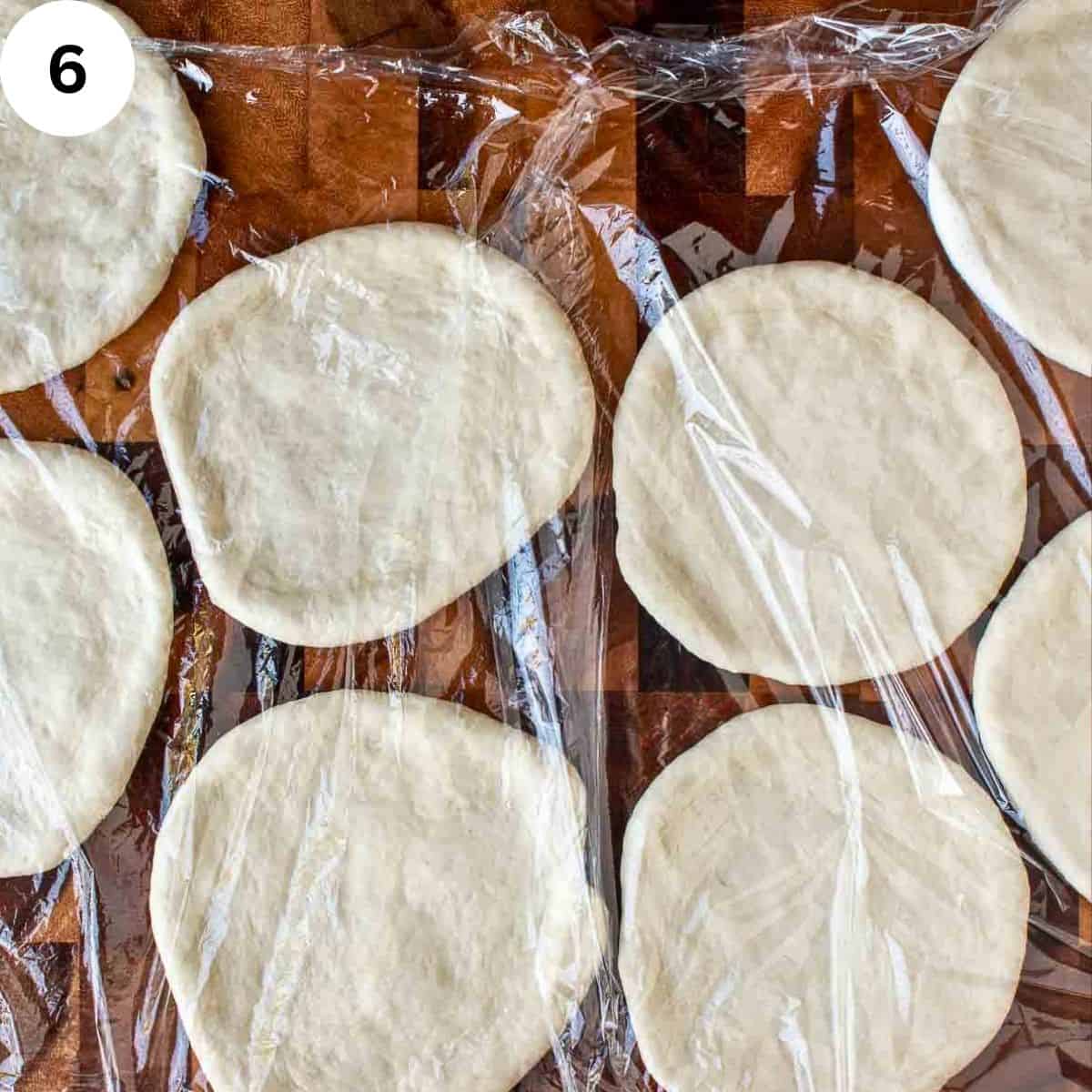 Discs of yeasted dough proofing under plastic wrap.