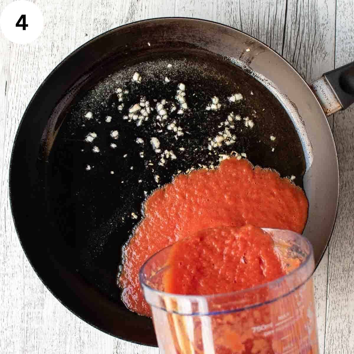 Pouring pureed tomato into a skillet with fried garlic.