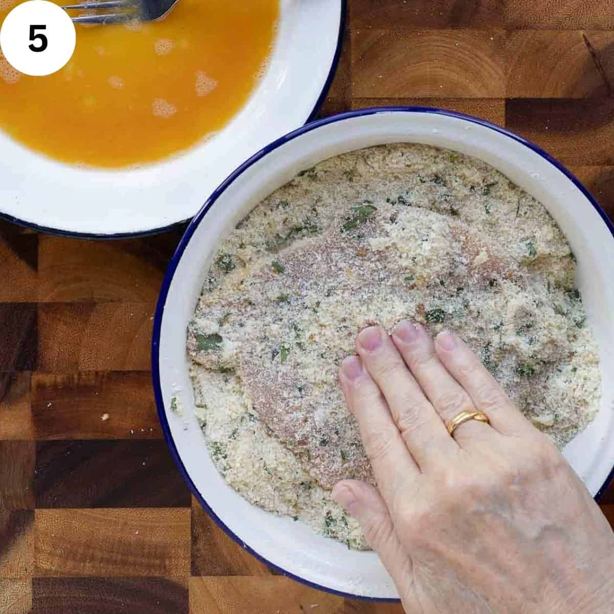 Pressing seasoned bread crumbs onto a cutlet.